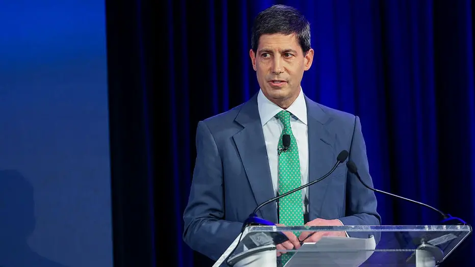 Kevin Warsh speaking at an event with a microphone and podium.