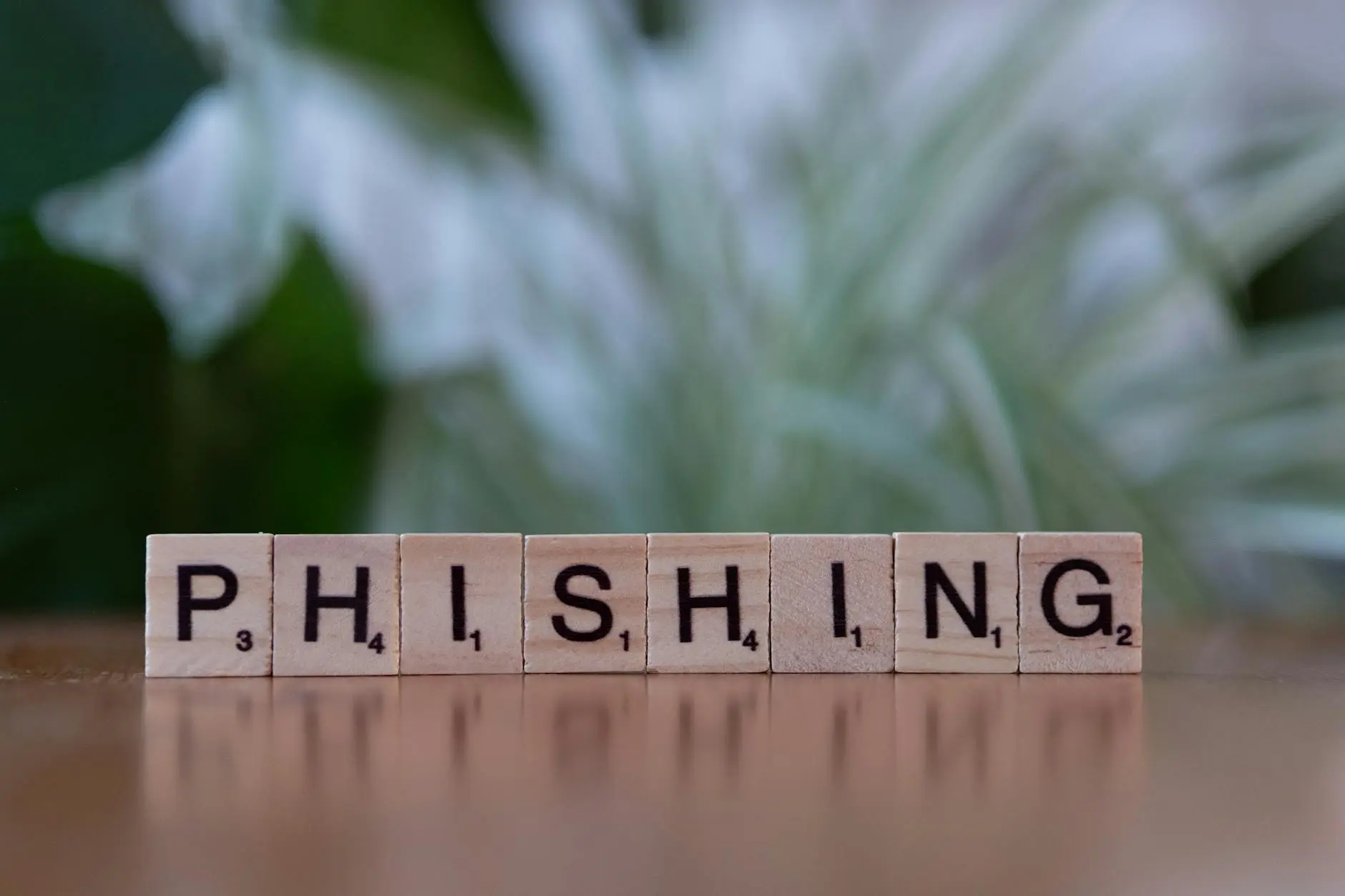 Scrabble tiles spelling out 'PHISHING' on a wooden surface with a blurred green background.