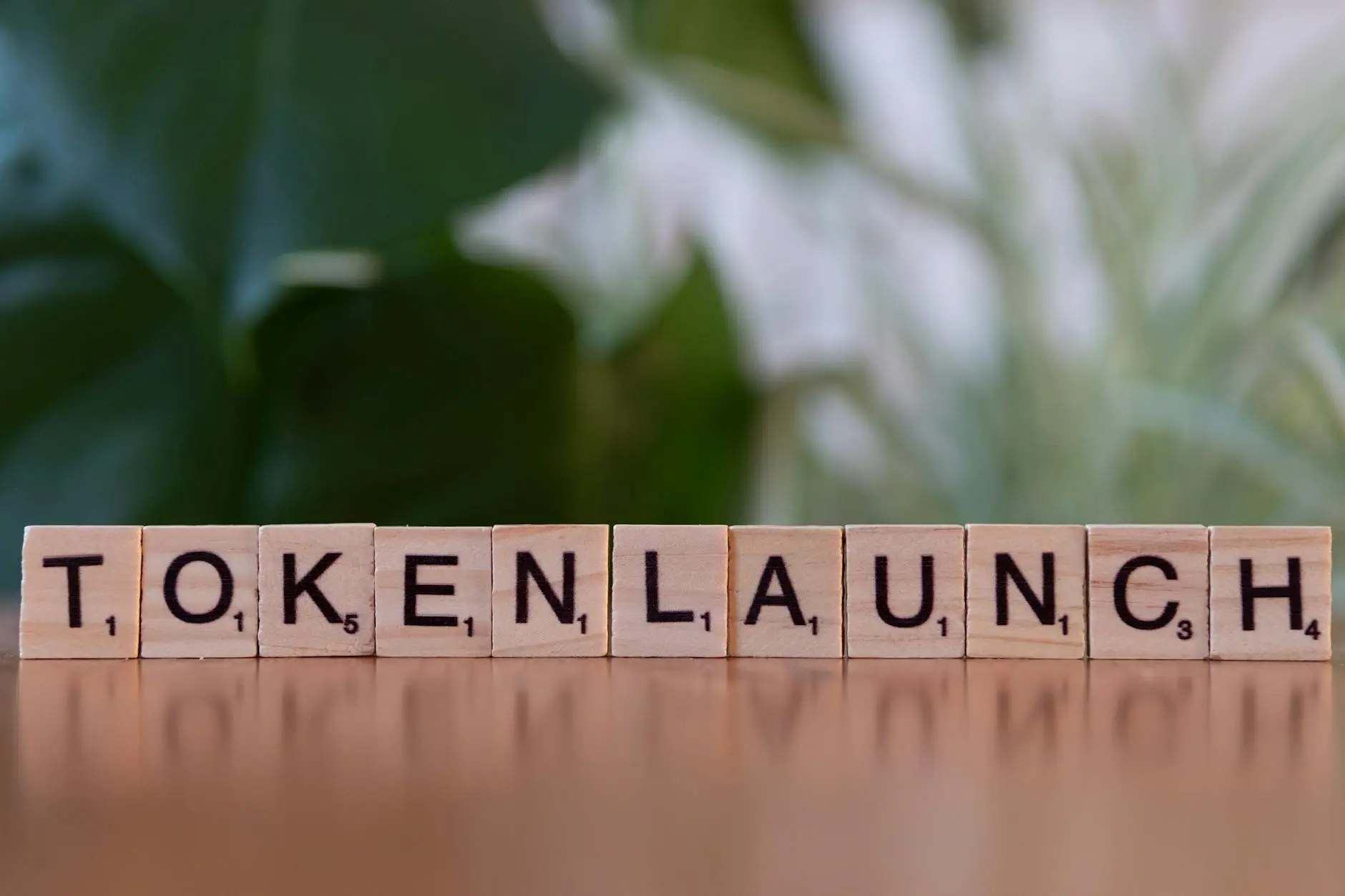 Scrabble tiles spell out 'TOKENLAUNCH' on a wooden surface with a blurred plant background.