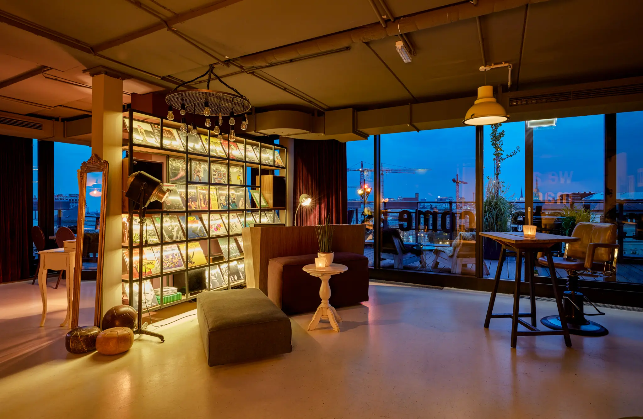 Cozy interior with a bookshelf, mirror, and window view of the city at dusk.