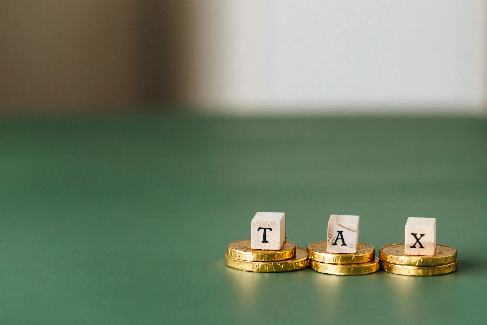 Wooden blocks spelling 'TAX' on stacked gold coins on a green surface.