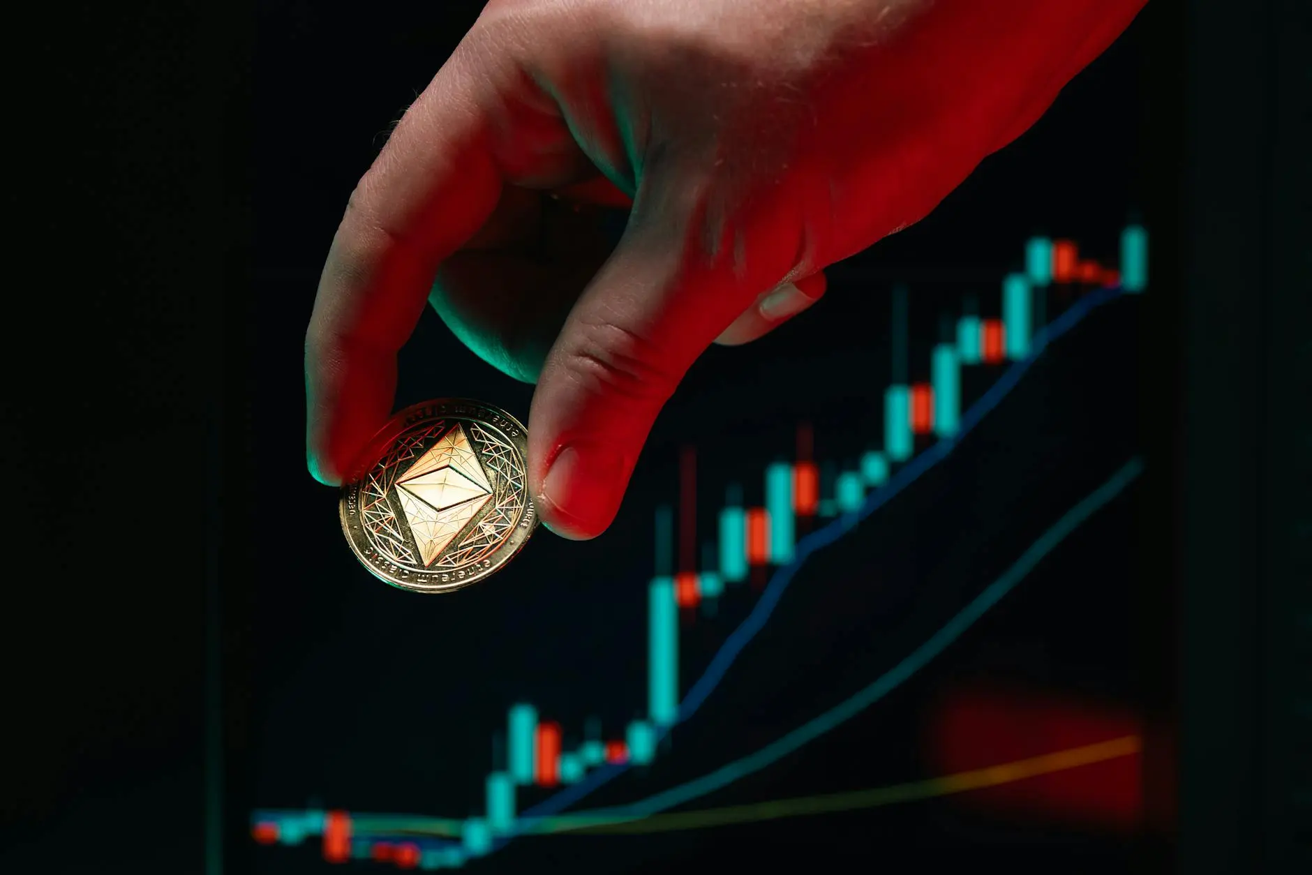 Eine Hand hält eine physische Ethereum-Münze vor einem Handelschart.