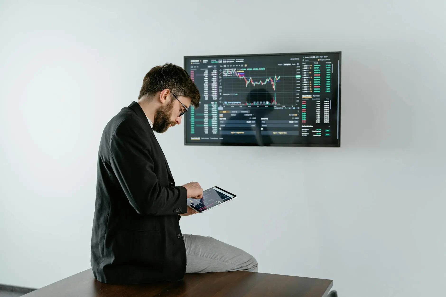 A crypto analyst using a tablet in front of data screens displaying market charts.