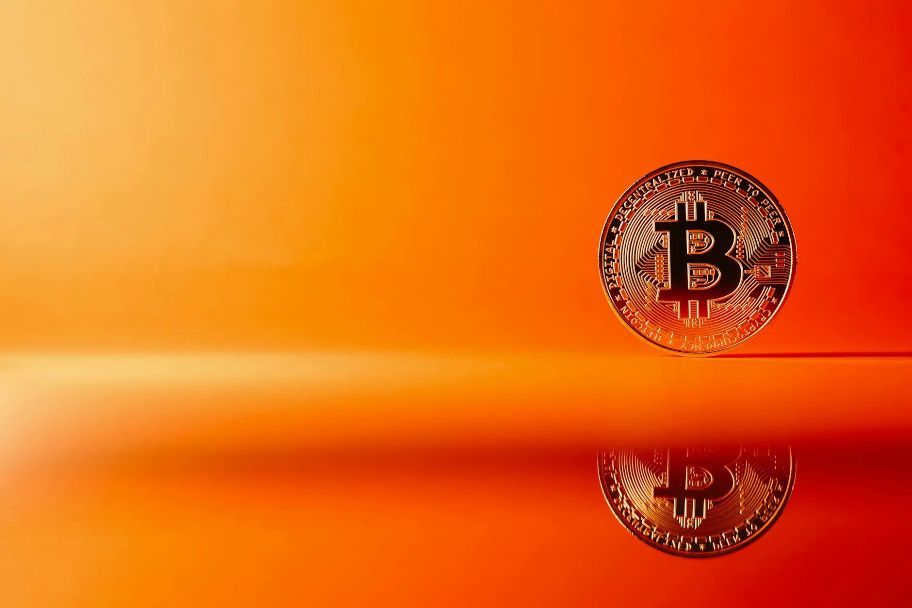 A Bitcoin coin reflecting on a smooth surface with an orange background.