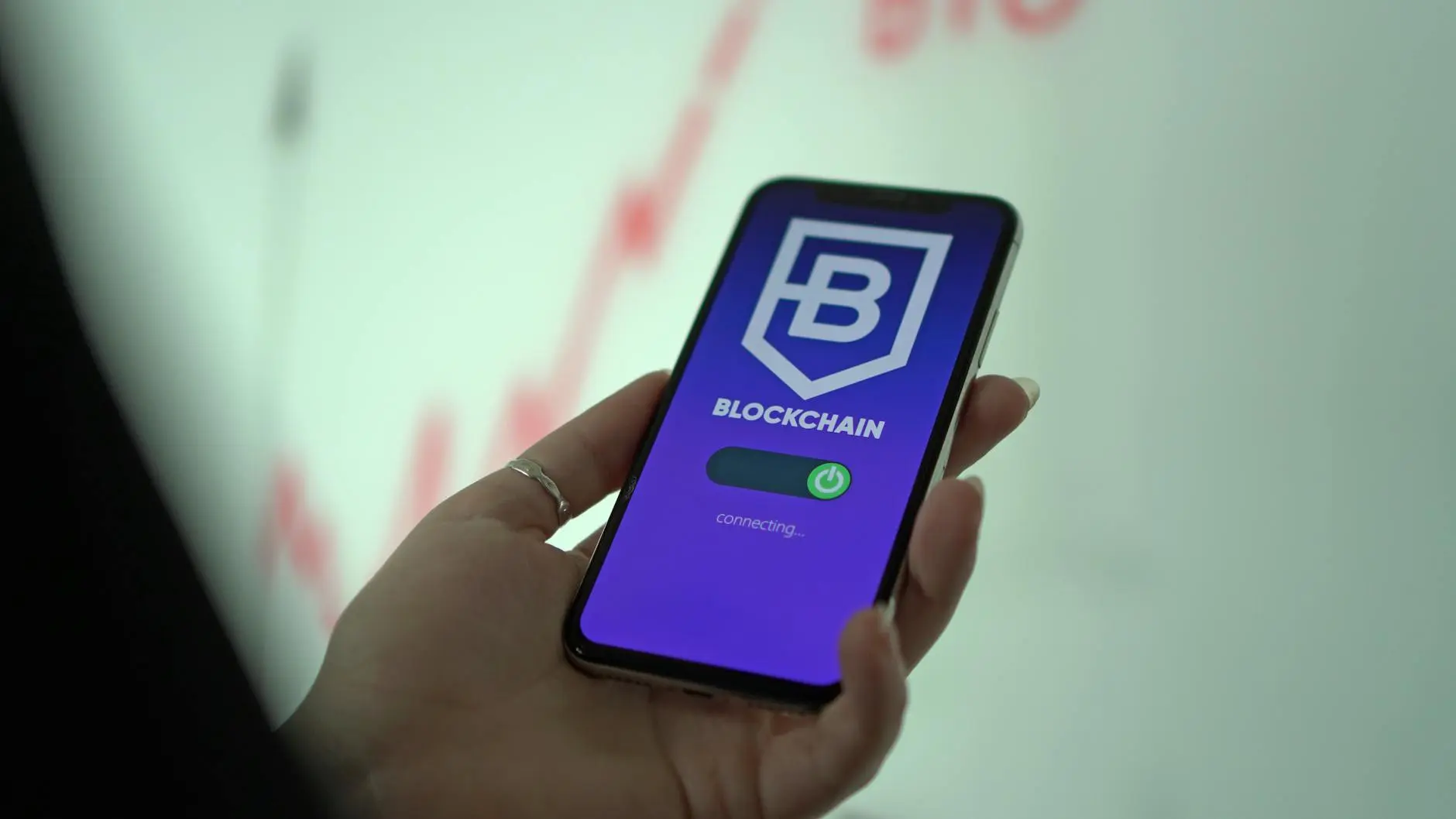 A hand holding a smartphone displaying a blockchain application interface.