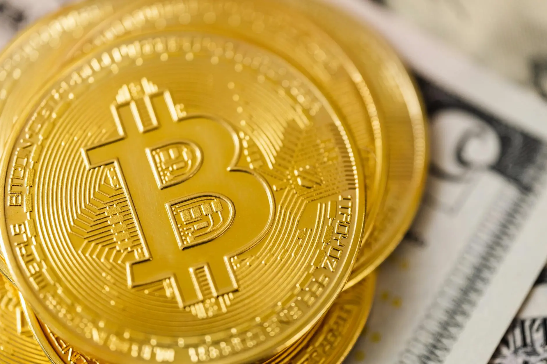 Close-up of Bitcoin coins on top of a stack of dollar bills.
