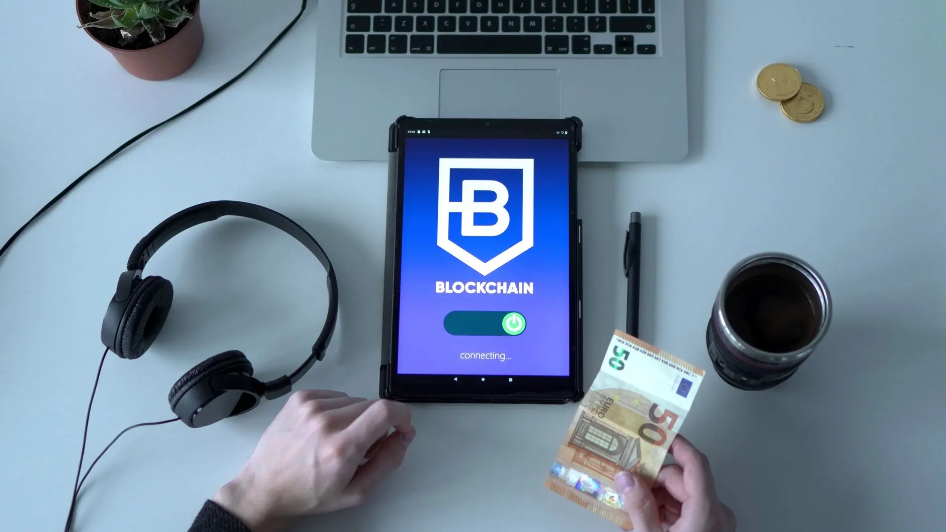 Tablet displaying blockchain interface with cash and laptop on a desk.