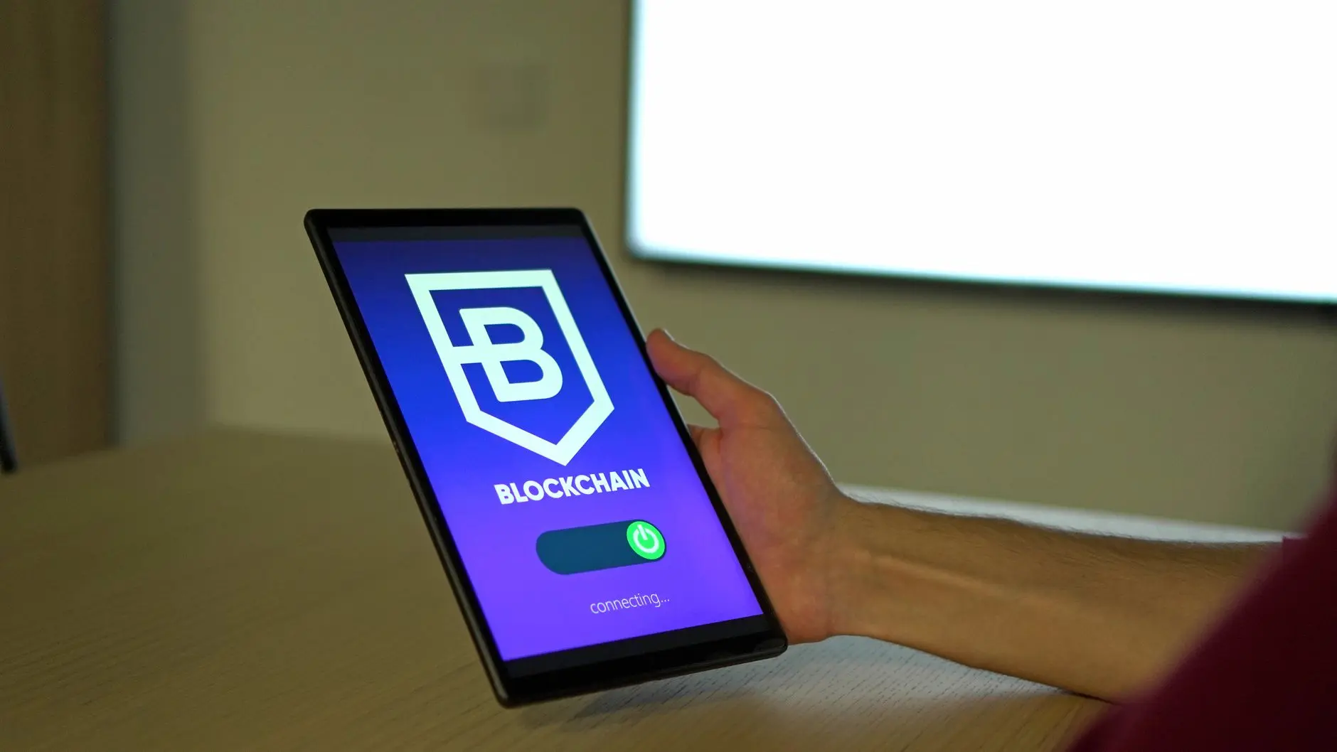 A hand holding a tablet showing a blockchain logo with a connecting status.