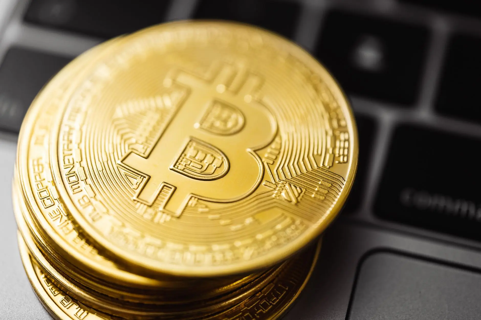 A stack of shiny gold Bitcoin coins resting on a keyboard.