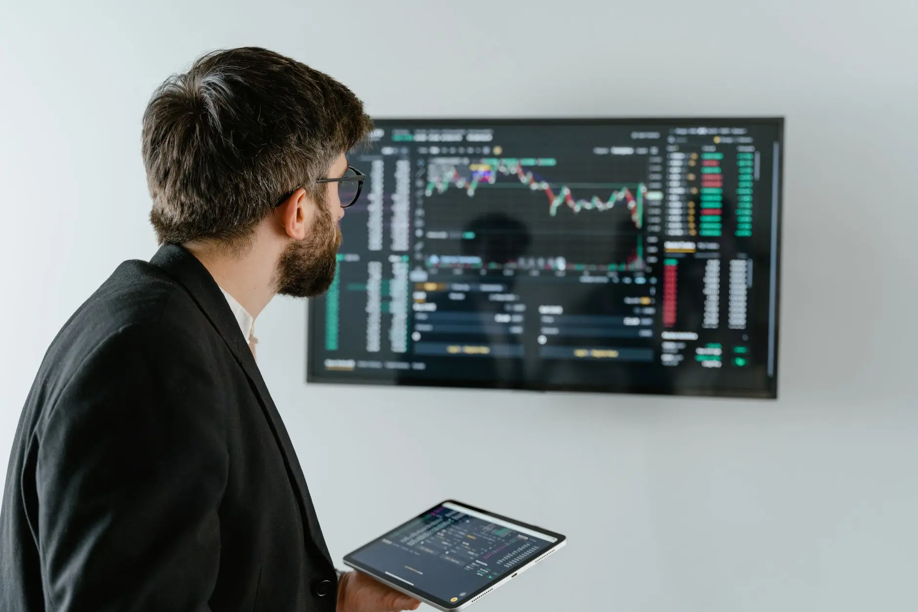 A man in a suit analyzing trading data on a screen with a tablet in his hand.