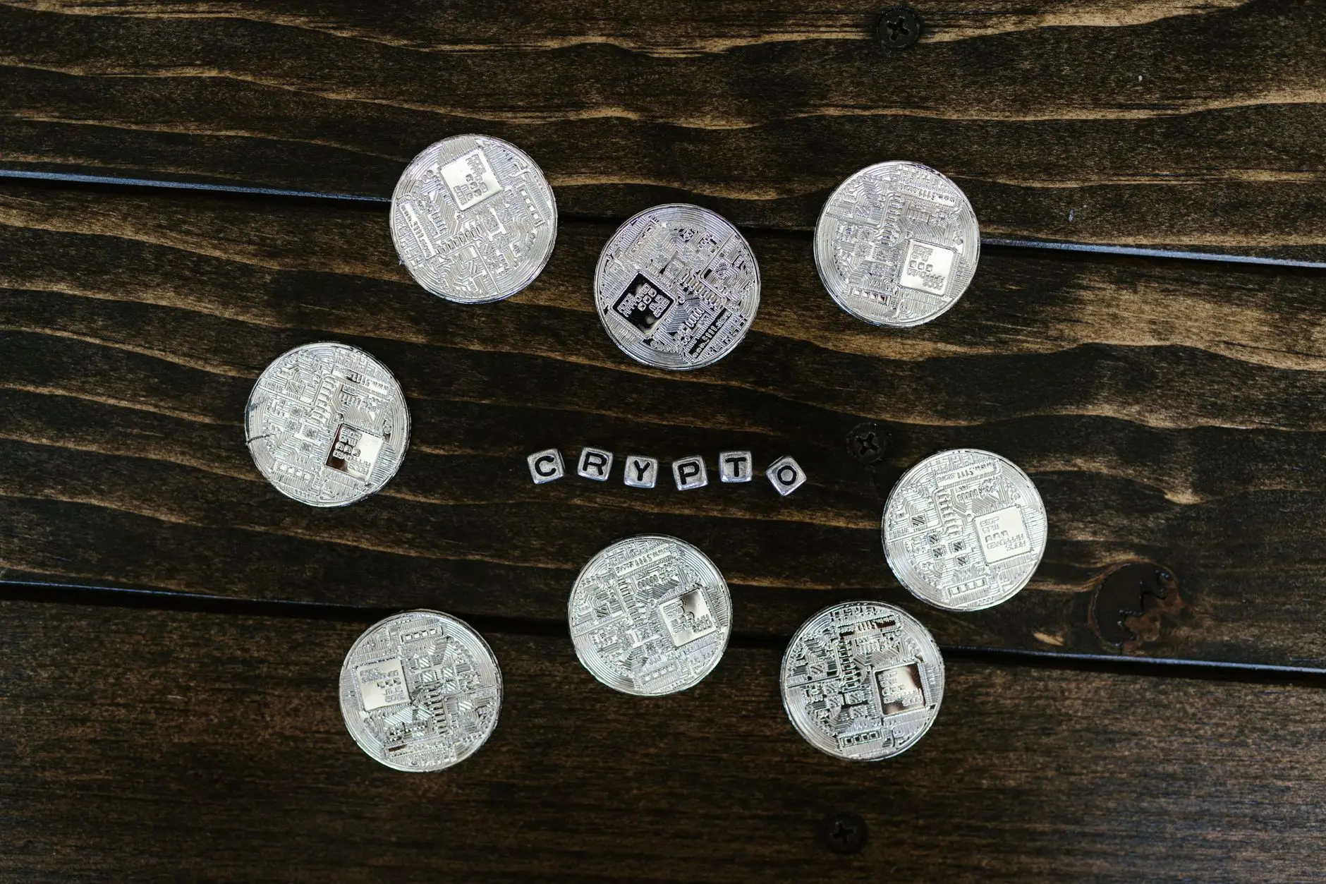 Silver crypto coins arranged on a wooden surface, with the word 'CRYPTO' spelled out.