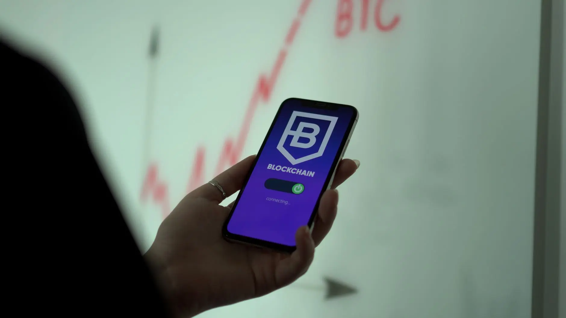 A hand holding a smartphone displaying a blockchain app interface.
