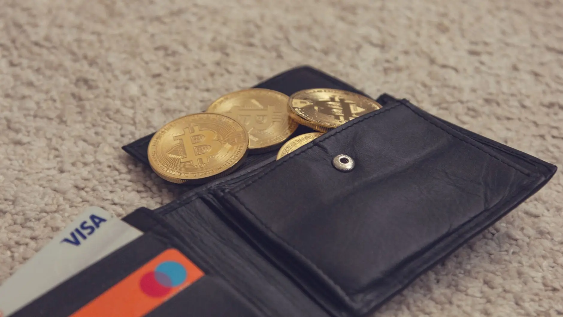 A black wallet with gold bitcoin coins and credit cards inside.