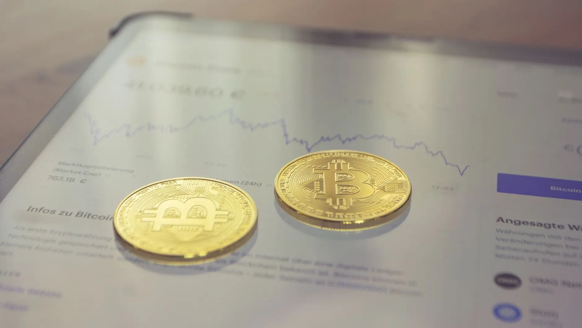 Two gold Bitcoin coins on a digital currency chart display.