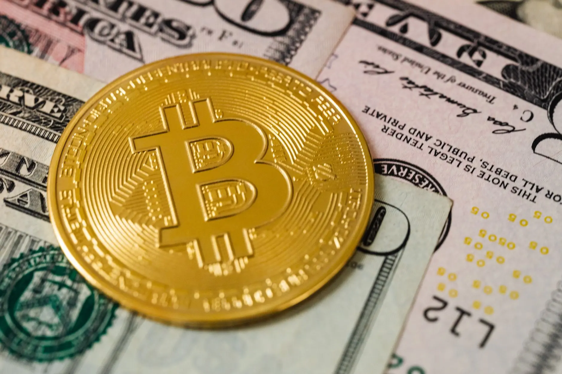 A Bitcoin coin resting on US dollar bills, illustrating financial concepts.