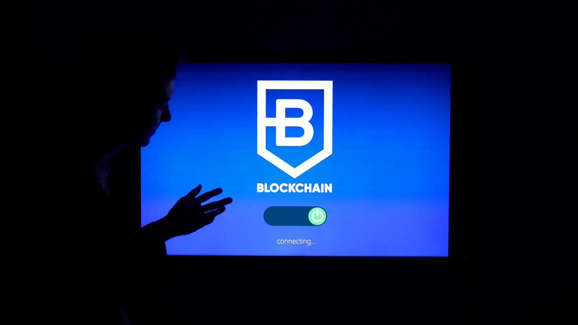 A silhouette of a person gesturing at a screen displaying a blockchain interface.