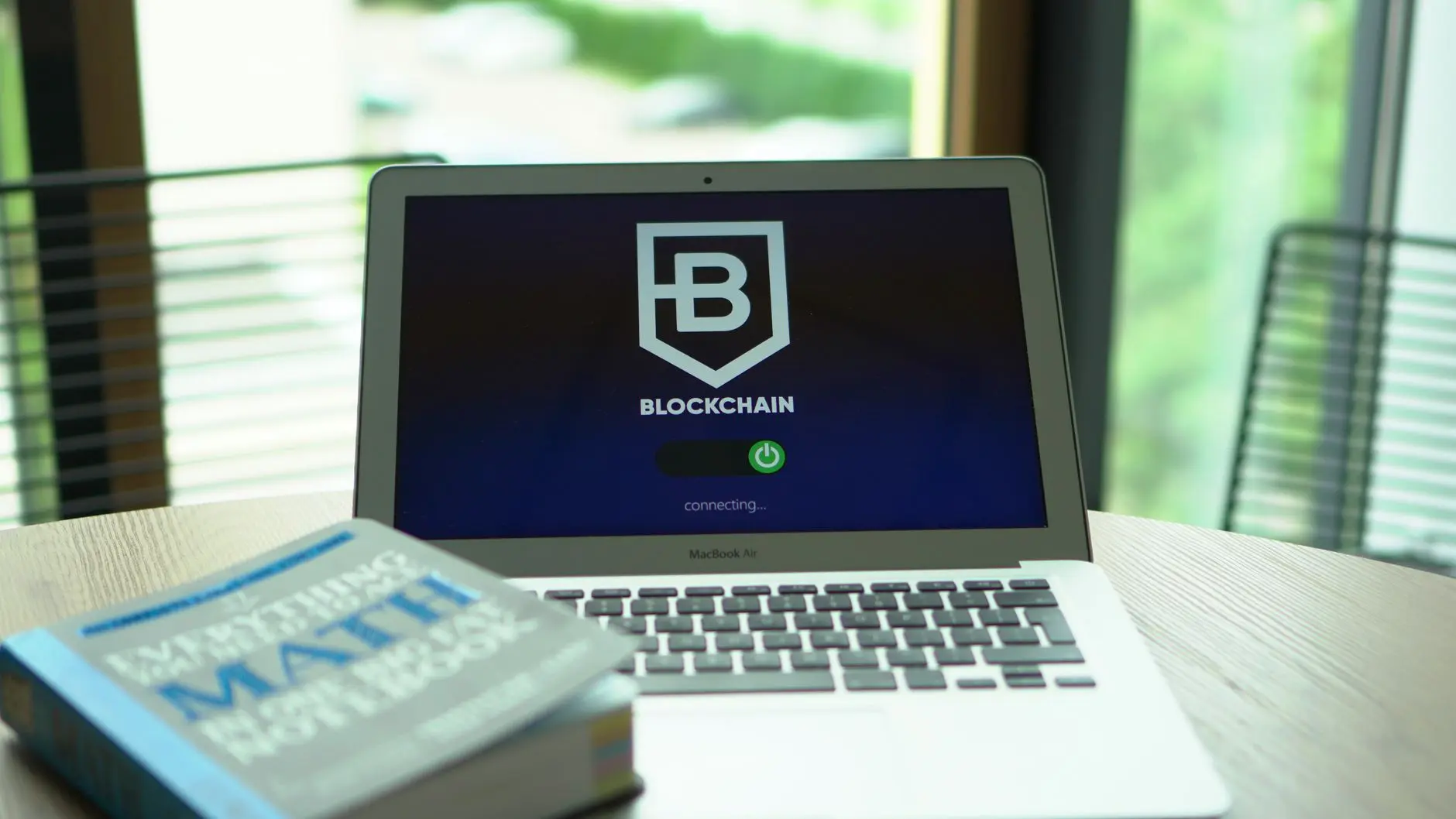 Laptop displaying a blockchain logo and loading screen with a math notebook beside it.