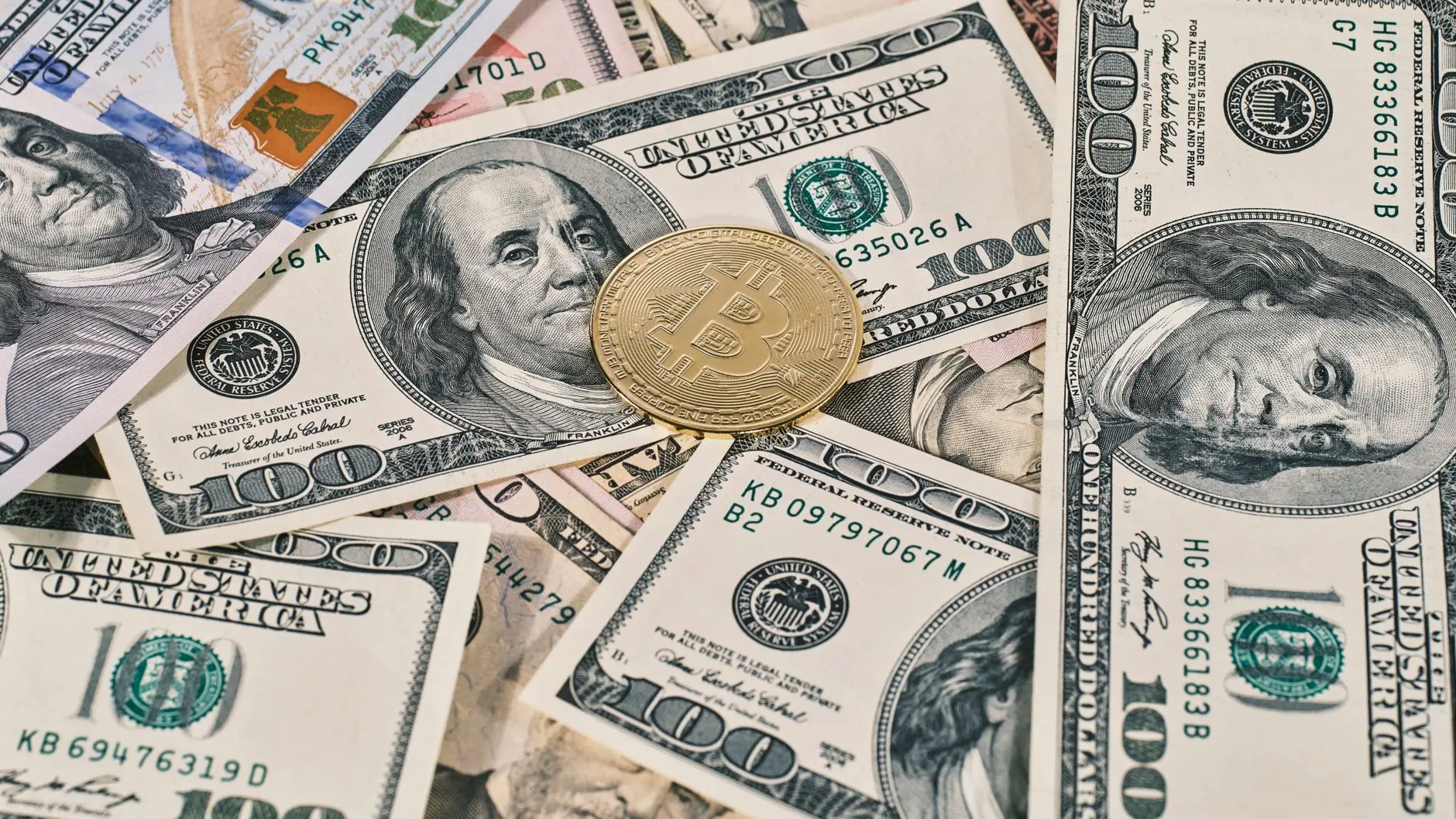A gold Bitcoin placed on US dollar bills, showcasing cash and cryptocurrency.
