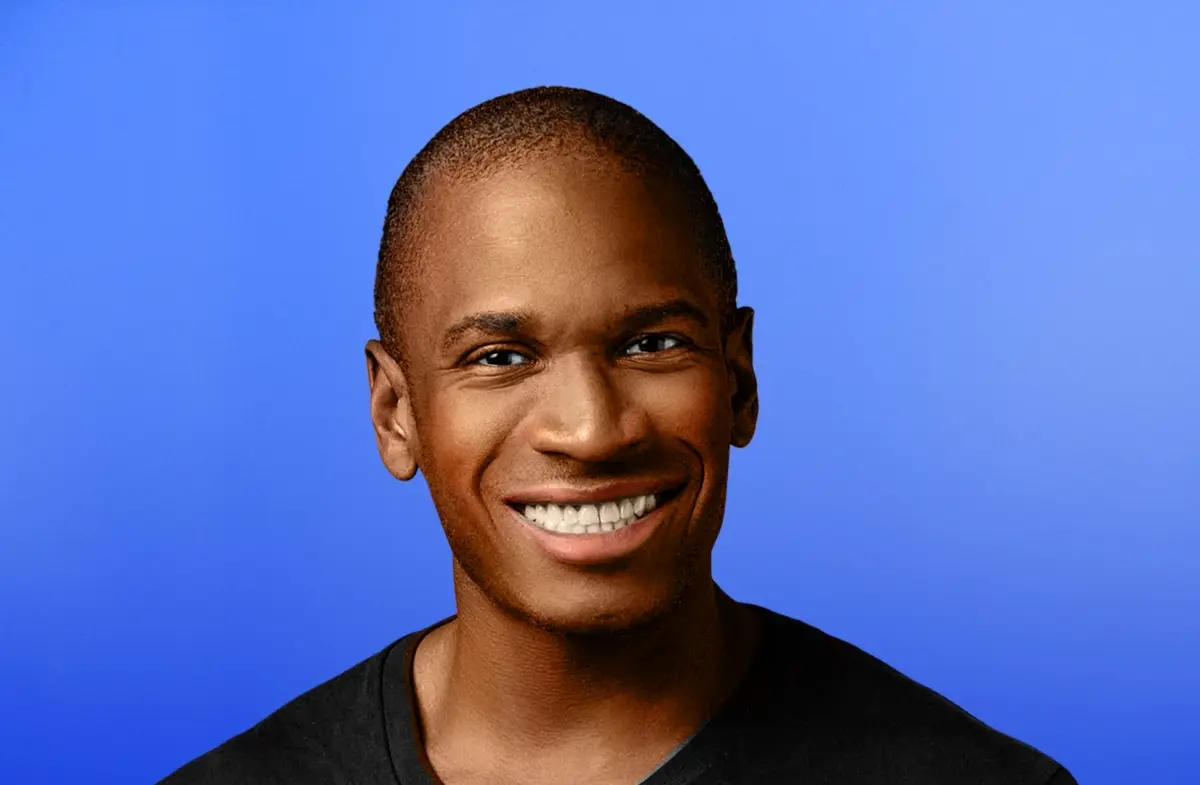 Smiling man with short hair against a blue background wearing a black shirt.