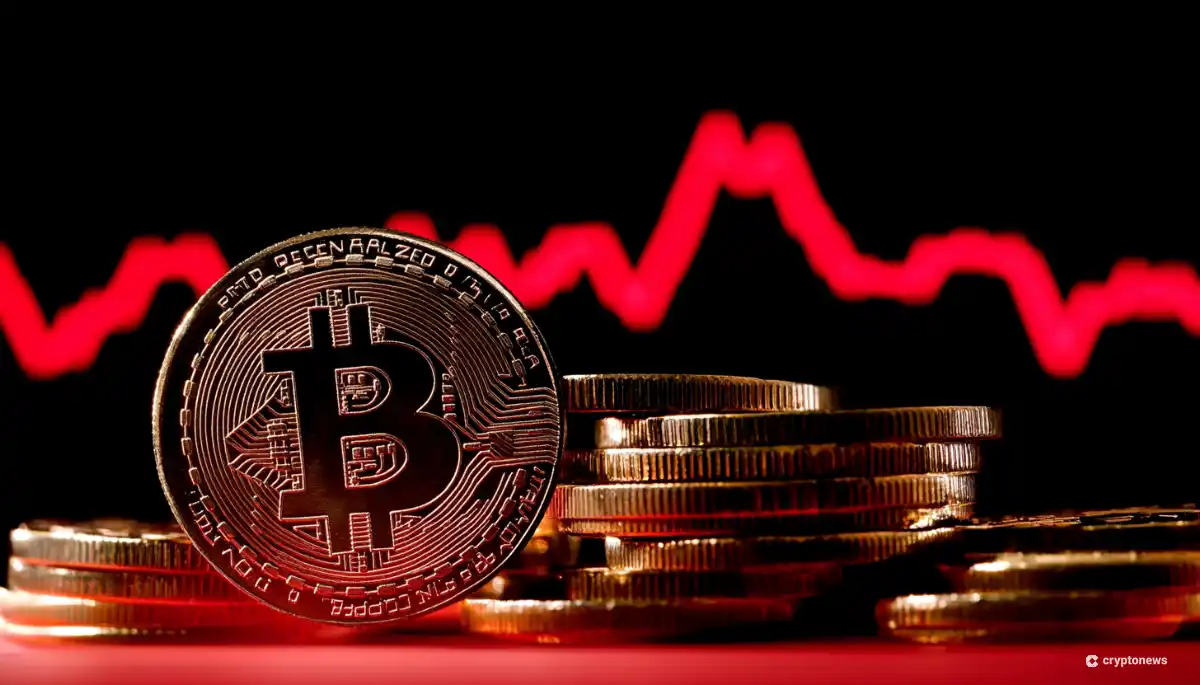赤いチャートを背景に、金色のビットコインコインが積み重ねられたコインの横に立てられている。黒い背景に赤い価格チャートのラインが変動を示し、暗号通貨市場のボラティリティを表現している