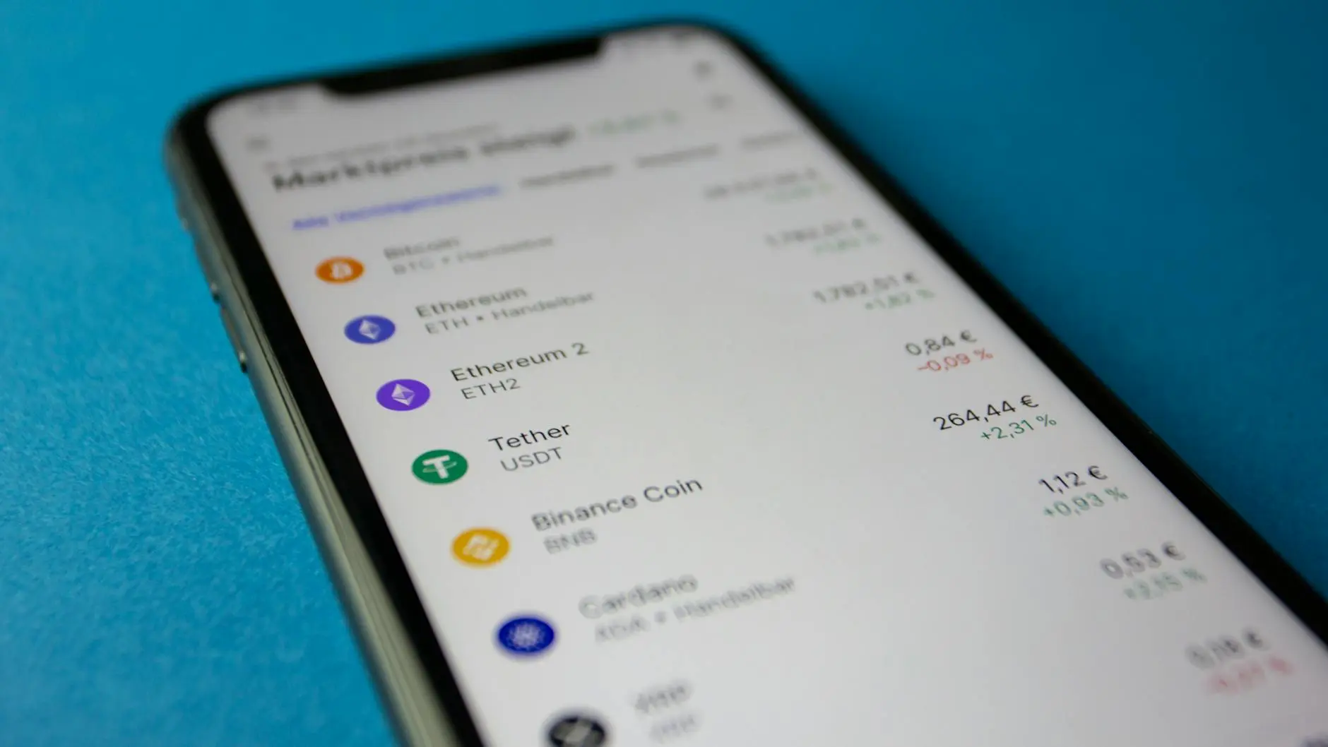 Close-up of a smartphone displaying cryptocurrency trading app interface with various cryptocurrencies listed.