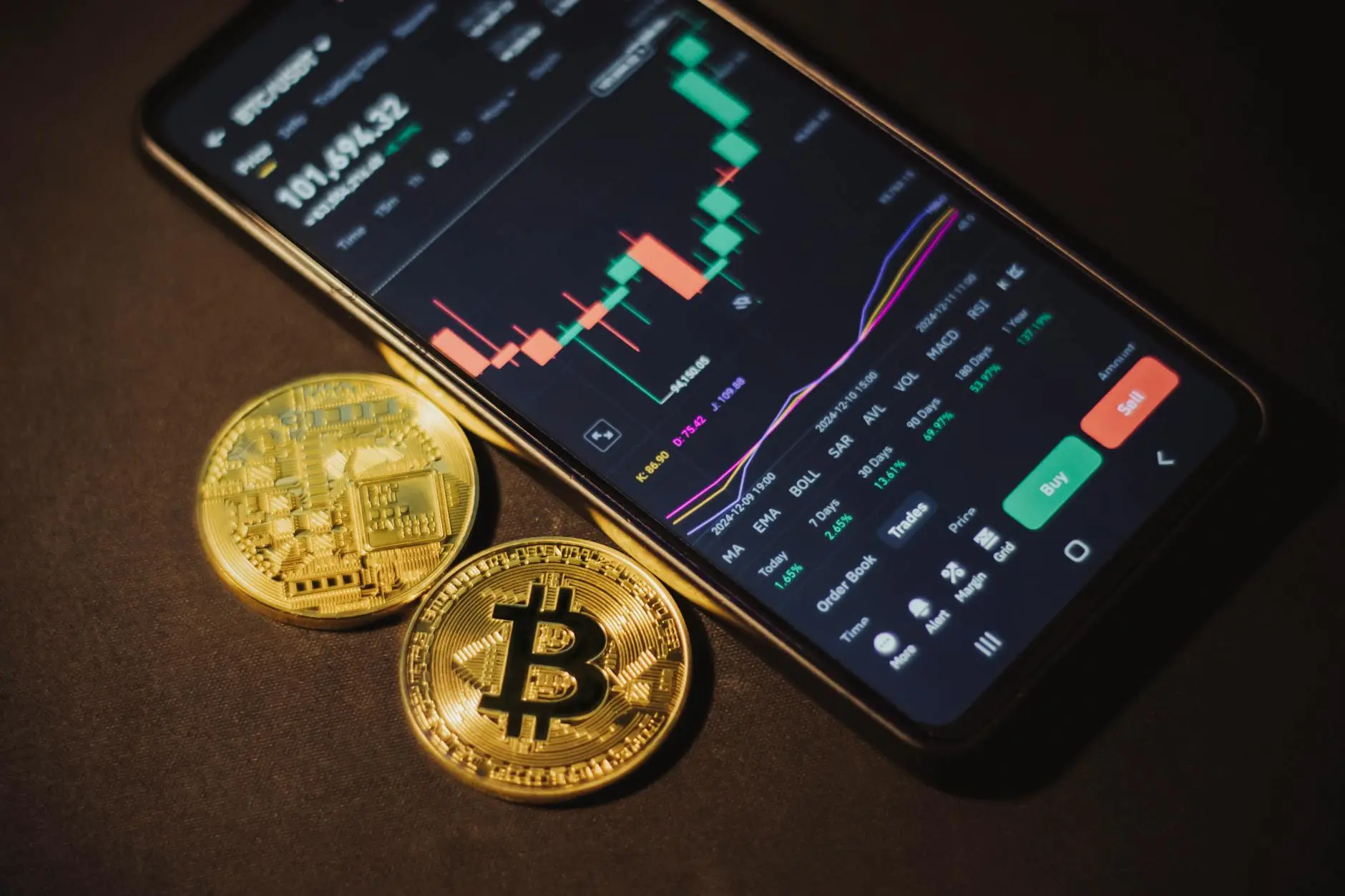 Smartphone displaying cryptocurrency market data with Bitcoin coins beside it.
