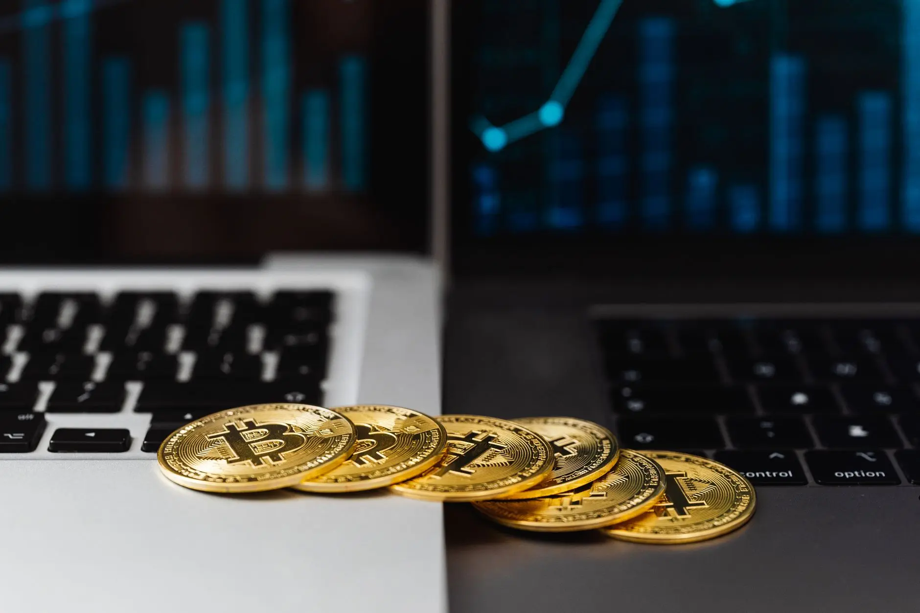Several Bitcoin coins placed on a laptop keyboard with a digital graph in the background.