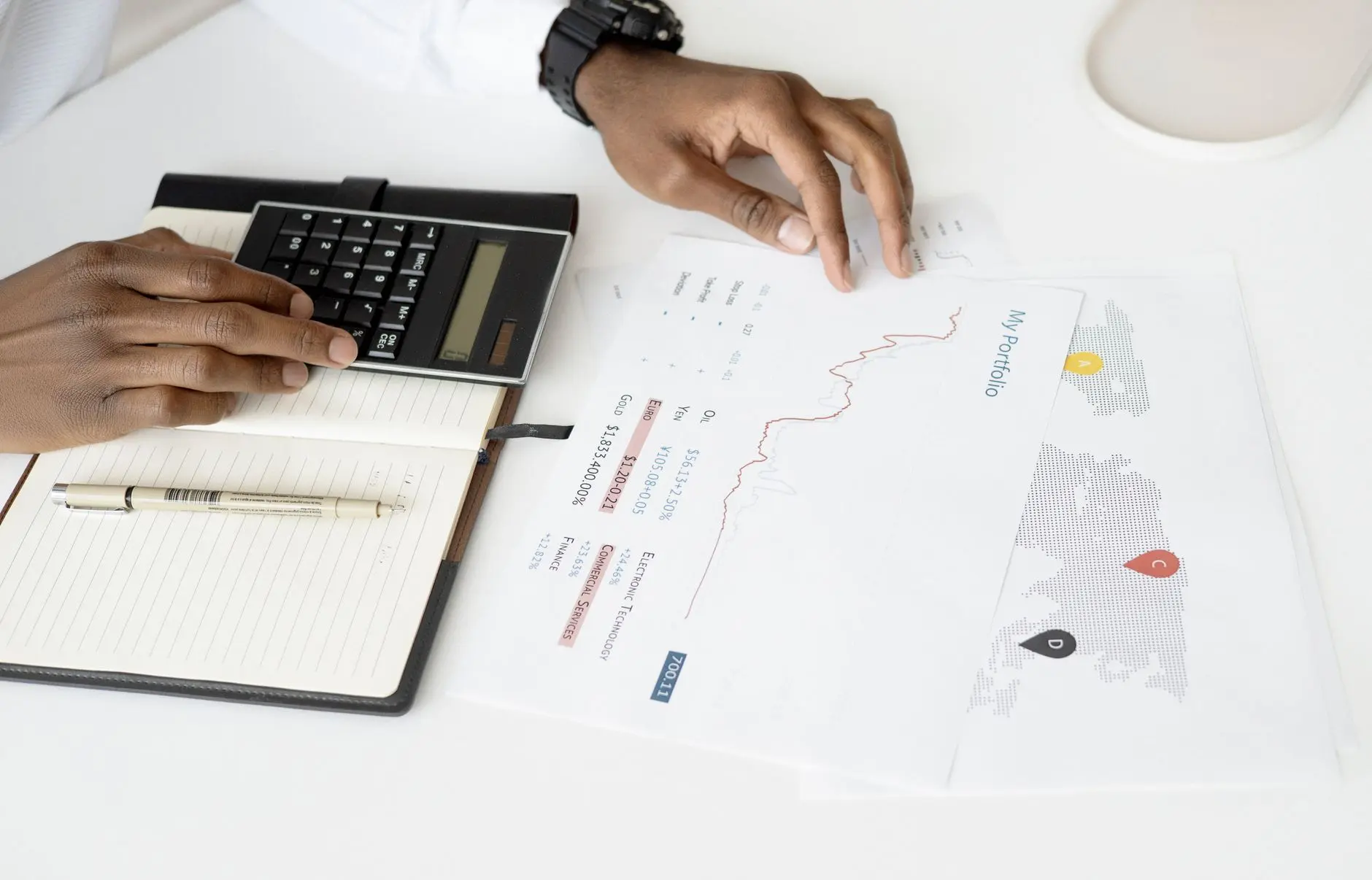 A hand analyzing investment charts with a calculator and notebook.