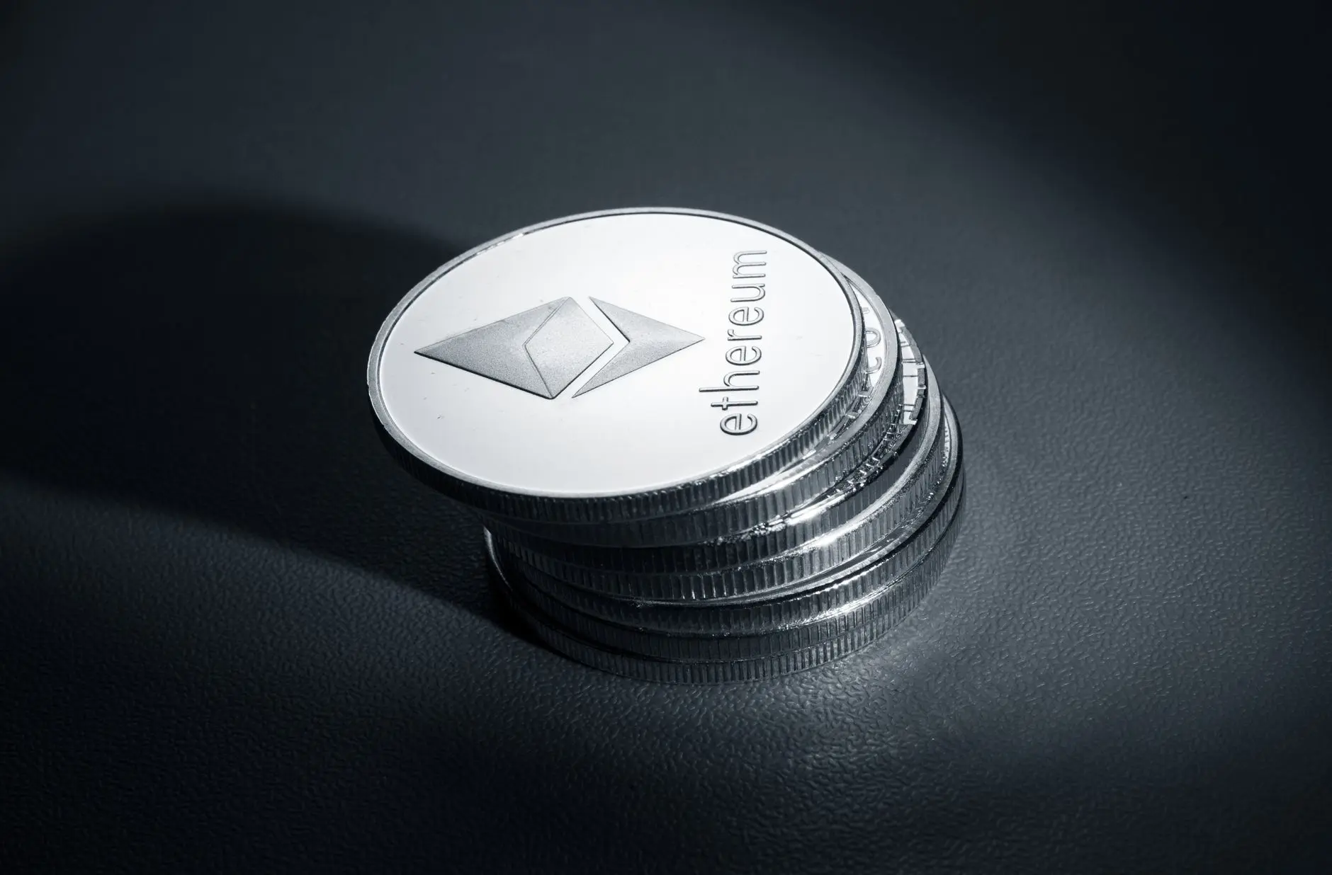 Silver Ethereum coins stacked on a black surface with logo visible.